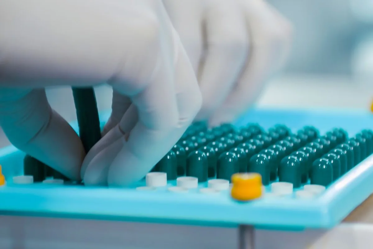 Gloved quality control specialist inspecting pharmaceutical capsules in a laboratory